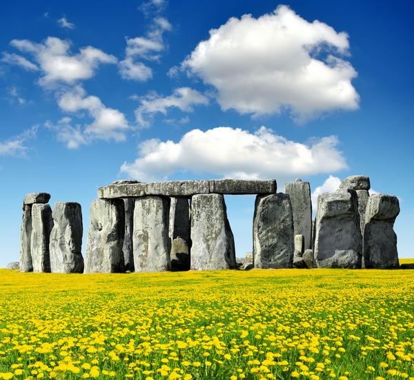 Stonehenge with yellow flowers in foreground against a blue sky with white clouds