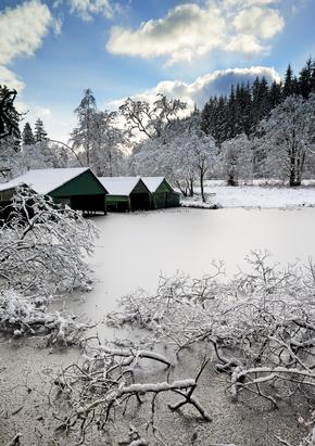 Boat houses on a frozen Loch Ard with frosted trees and branches strewn over the Loch