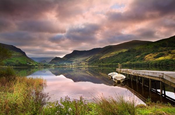 View of Snowdon covered in cloud at sunrise from Llyn Nantlle with reflections in lake and vibrant colors with rowing boats moored at jetty