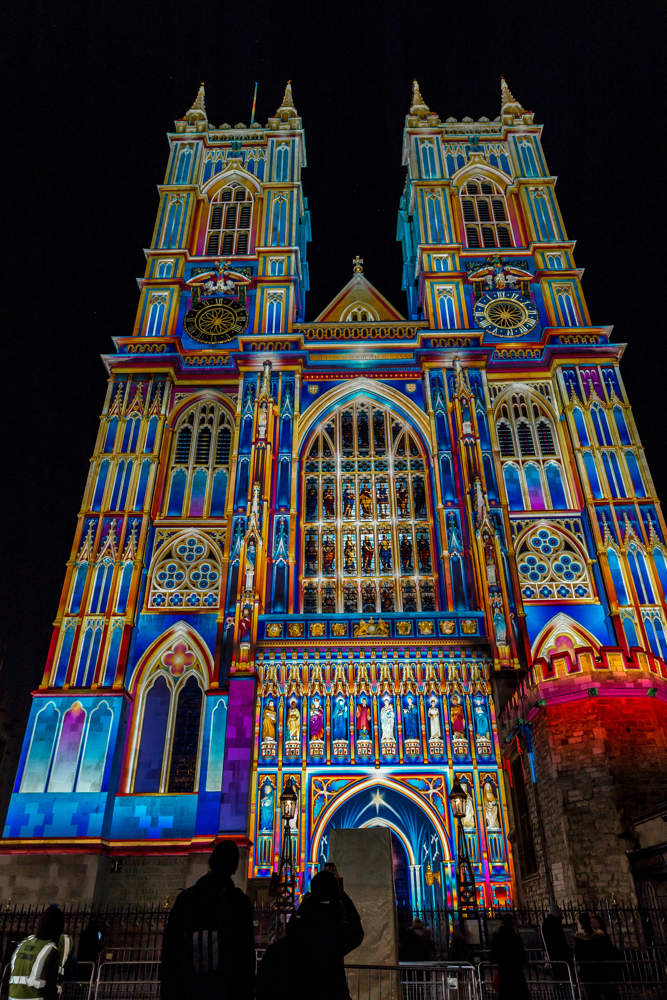 Outside of large abbey lit up at night with multi-coloured lights to make it look like a stained glass window