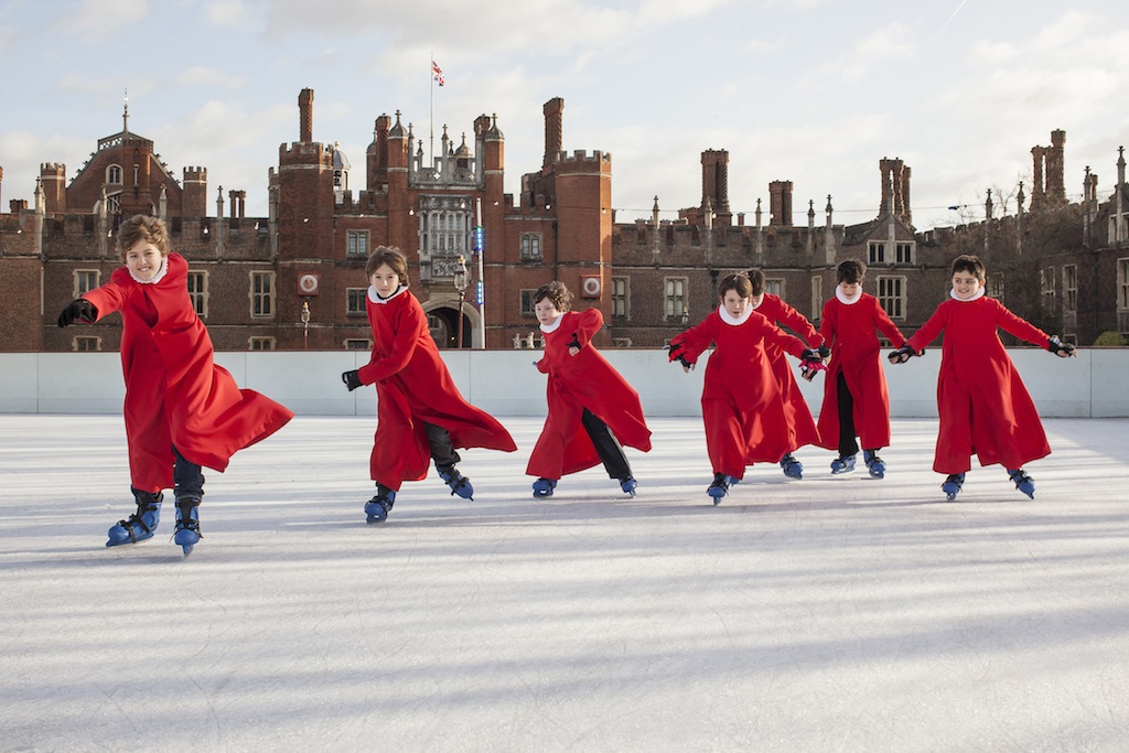 Choirboys wearing red gowns ice-skating towards the viewer