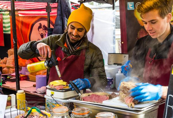 A man melting cheese on burgers using a blow torch at a stall in Camden Food Market