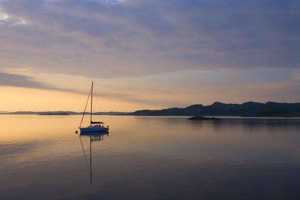 Tranquil photo of  a sailboat infront of the setting sun on Loch Crinan